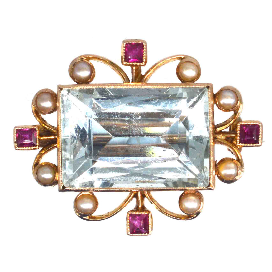 Edwardian 18ct gold brooch featuring aquamarine, ruby, and pearl in a vintage swirly design.