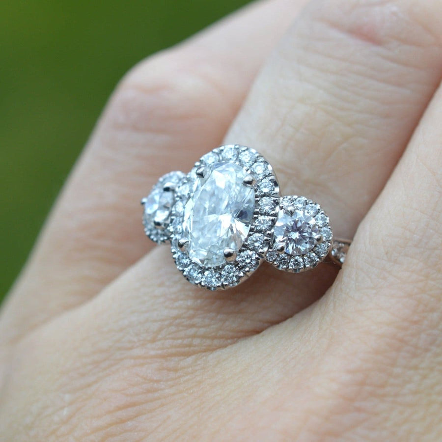 Modern three stone diamond cluster ring featuring a spectacular central oval diamond and two round stones.