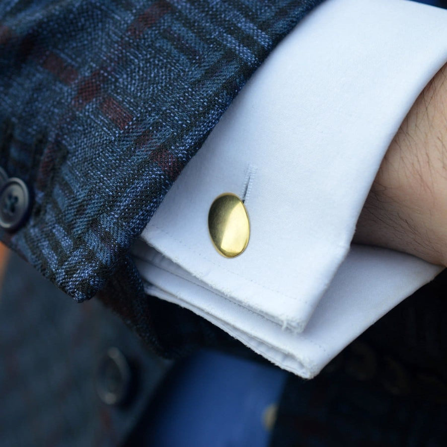 Close-up of a man's cuff with a plain gold oval cufflink showcasing classic Art Deco style.