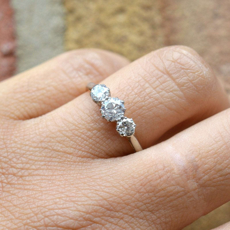Art Deco platinum and 18ct gold three stone diamond ring on a finger, showcasing brilliant clear diamonds.